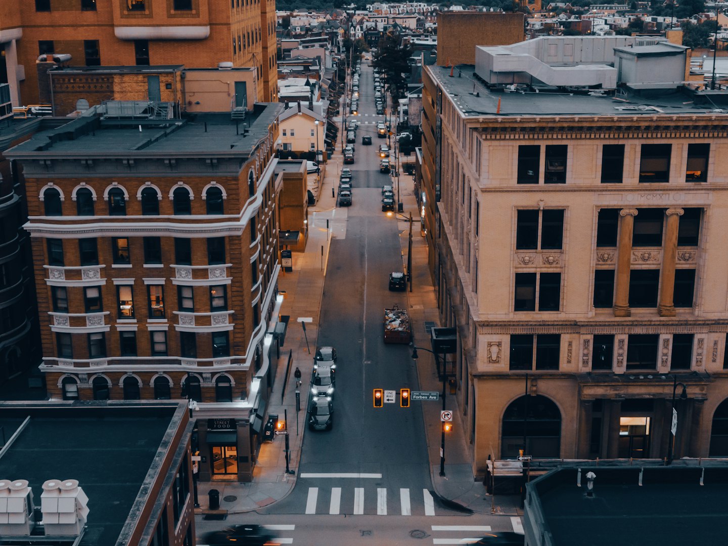 Aerial view of a quiet city street at dusk with illuminated streetlights.