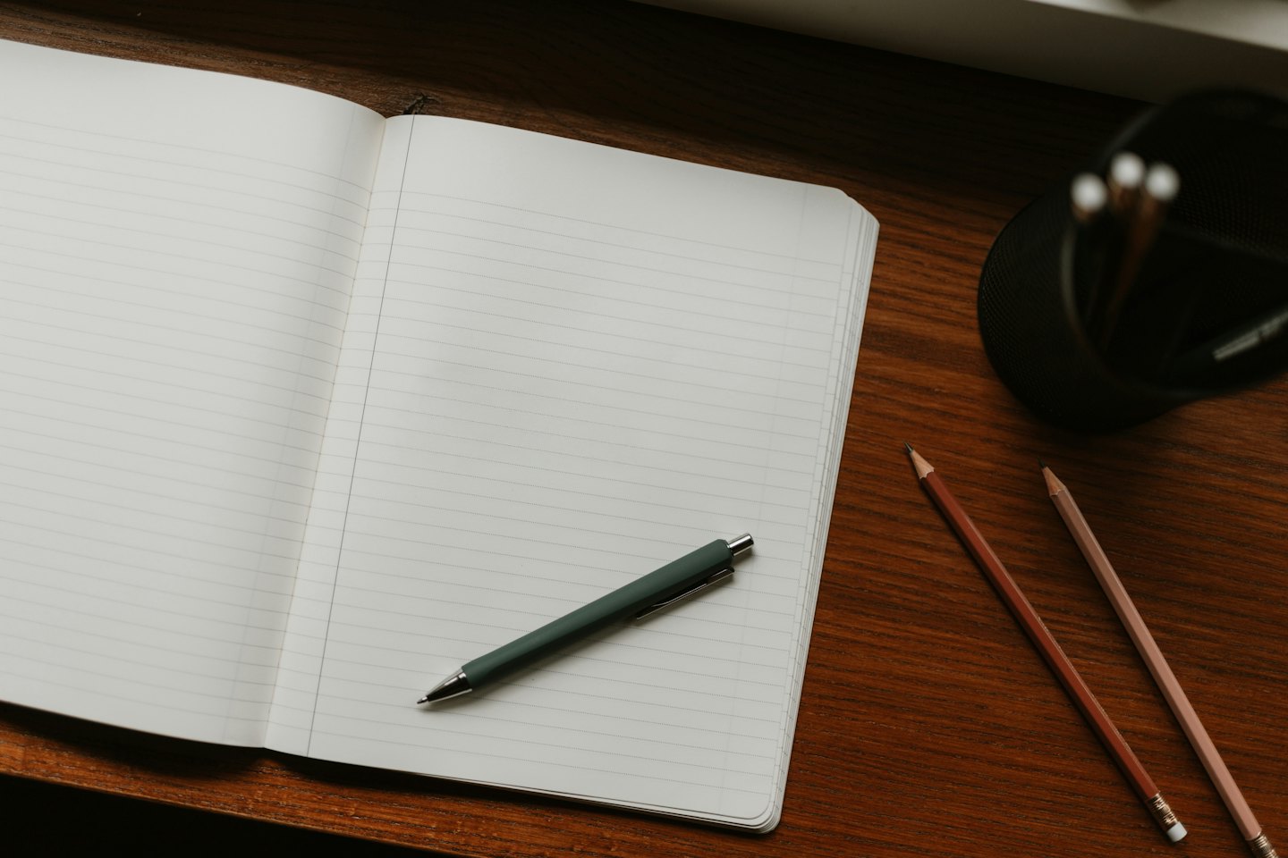 Open notebook with pen and colored pencils on wooden desk.